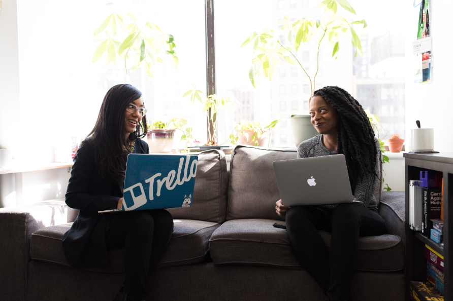 Two happy friends sitting on a couch using their laptops